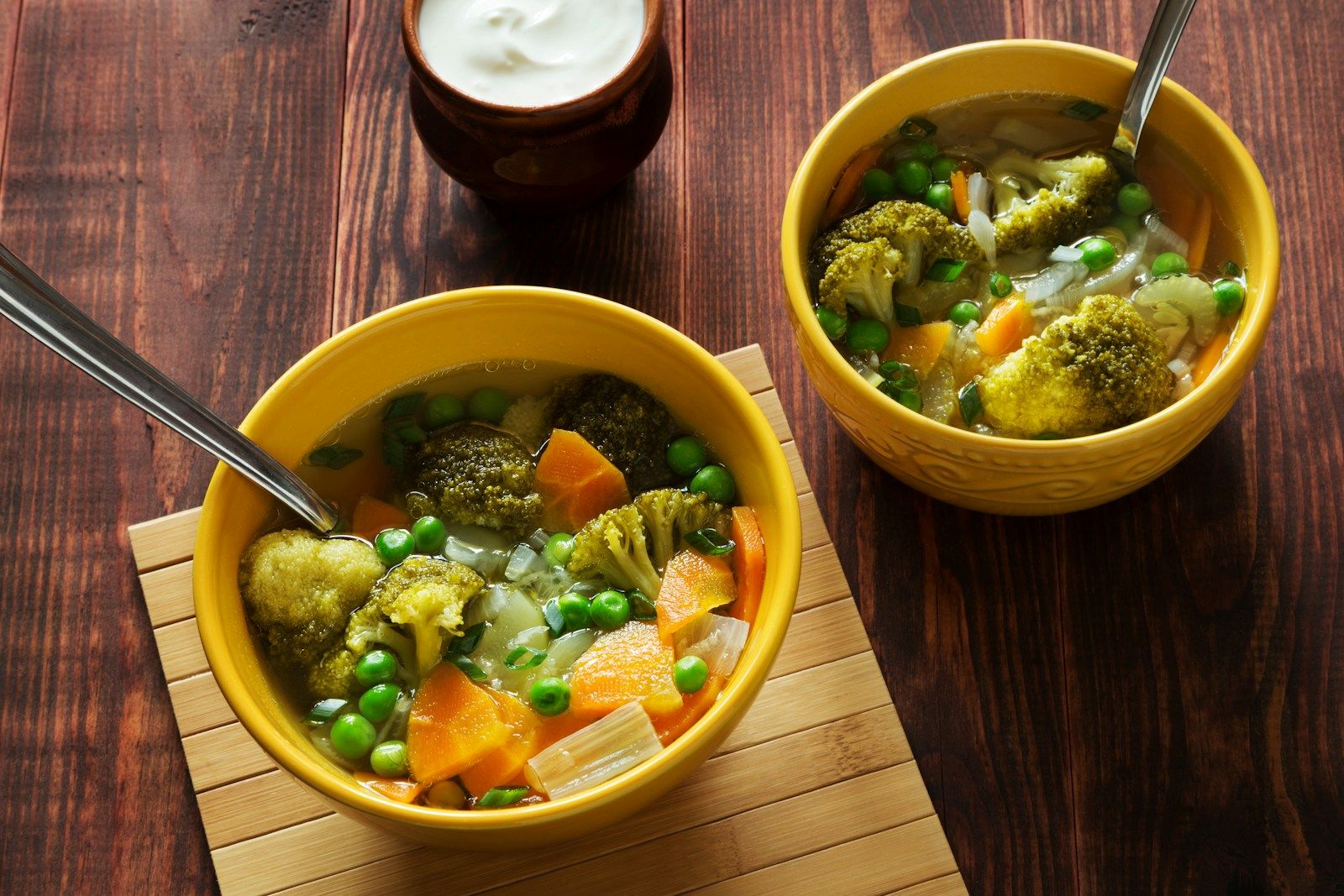 Zwei Schalen Gemüsesuppe mit Karotten, Erbsen und Brokkoli auf einem Holztisch