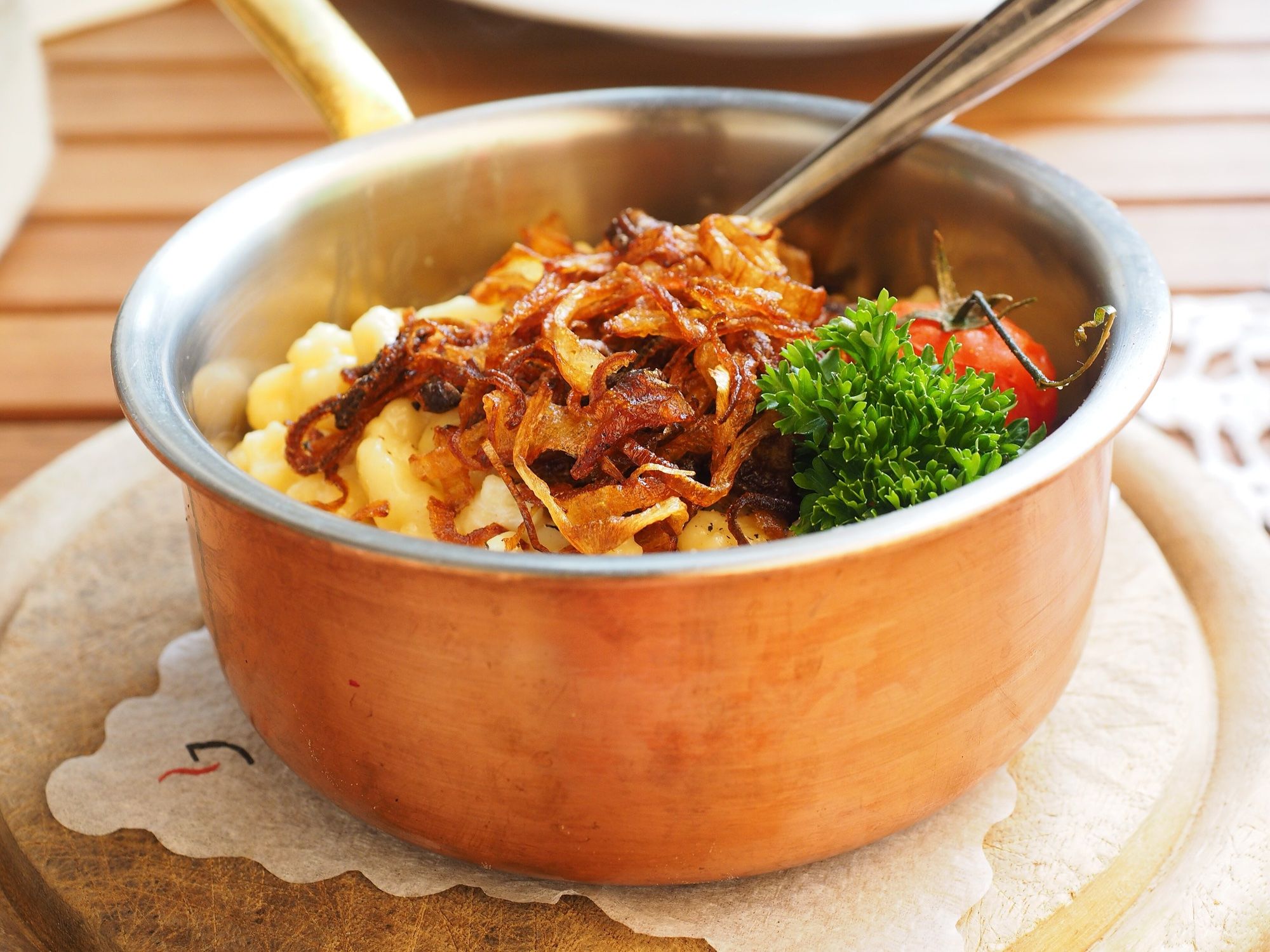 Käsespätzle in einem Kupfertopf, mit goldbraunen Röstzwiebeln bestreut