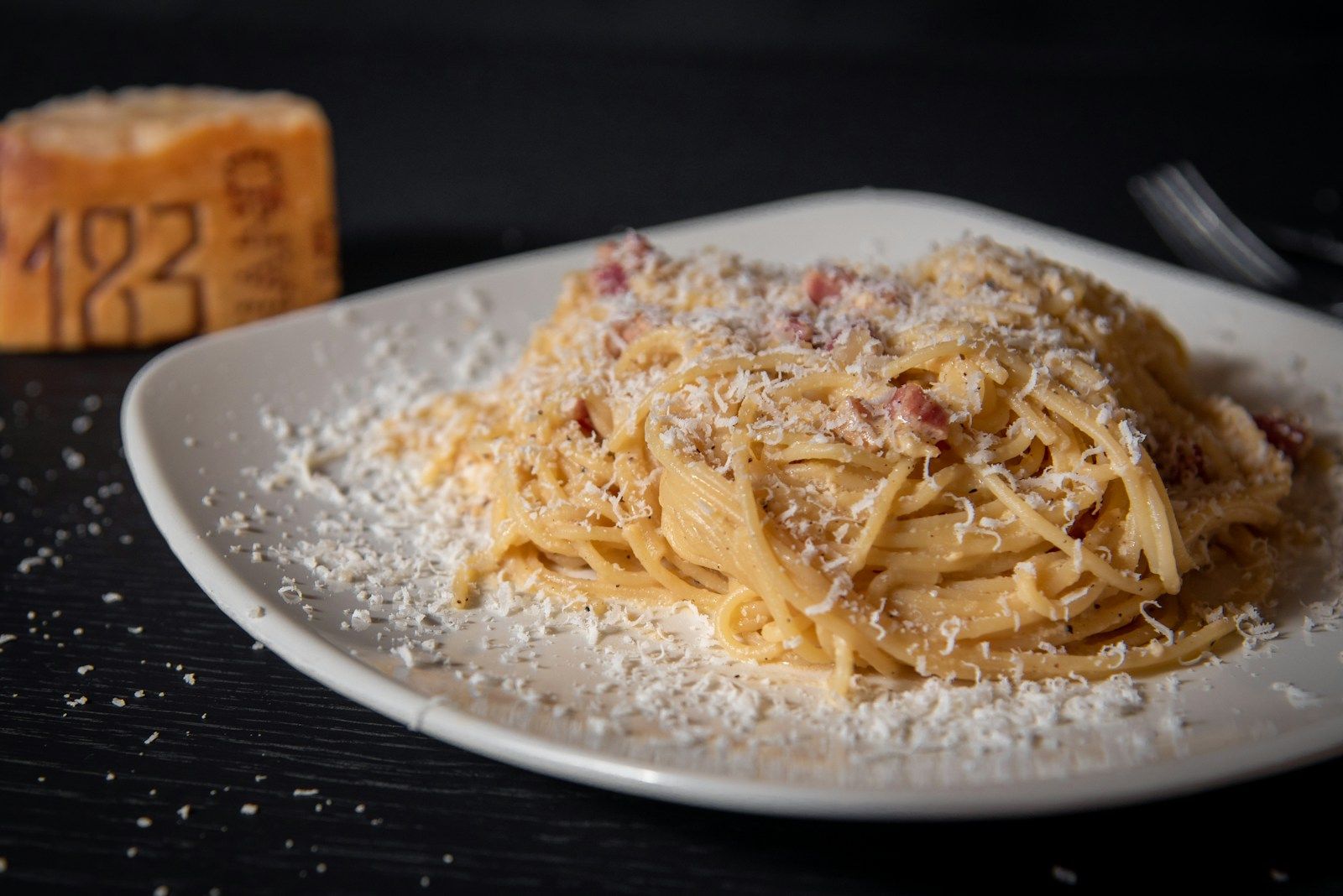 Spaghetti Carbonara mit Speck und reichlich geriebenem Pecorino auf einem weißen Teller